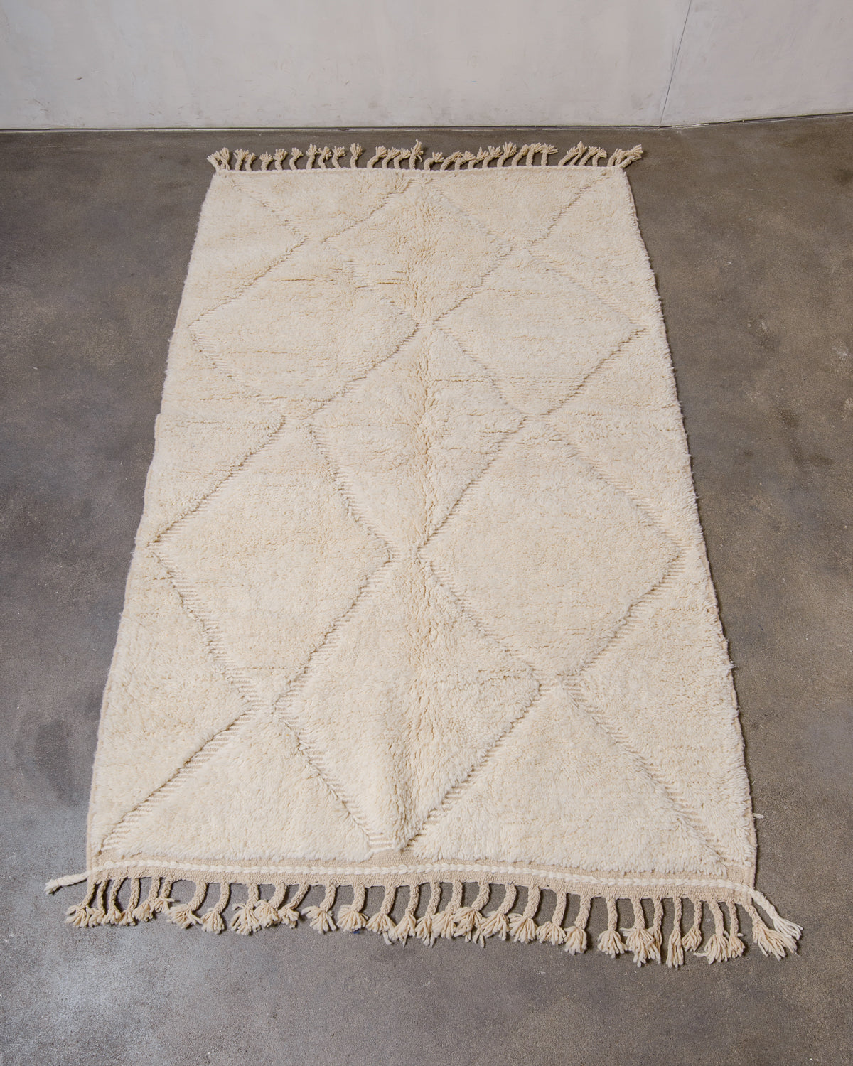 Berberlin Beniourain rug made of cream wool laying flat on concrete floor.